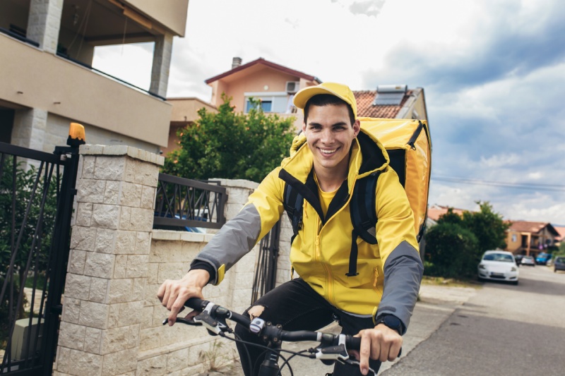 Livreur à vélo souriant | TRANSPORT INTER-REGIONAL Livreur à vélo en tenue jaune dans une rue résidentielle